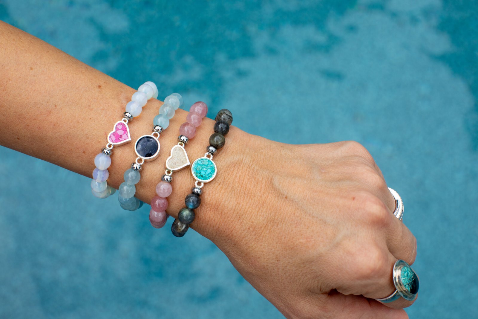 Shot of wrist against blue background, wearing four beaded bracelets stacked. The perfect gift for Mother's Day.